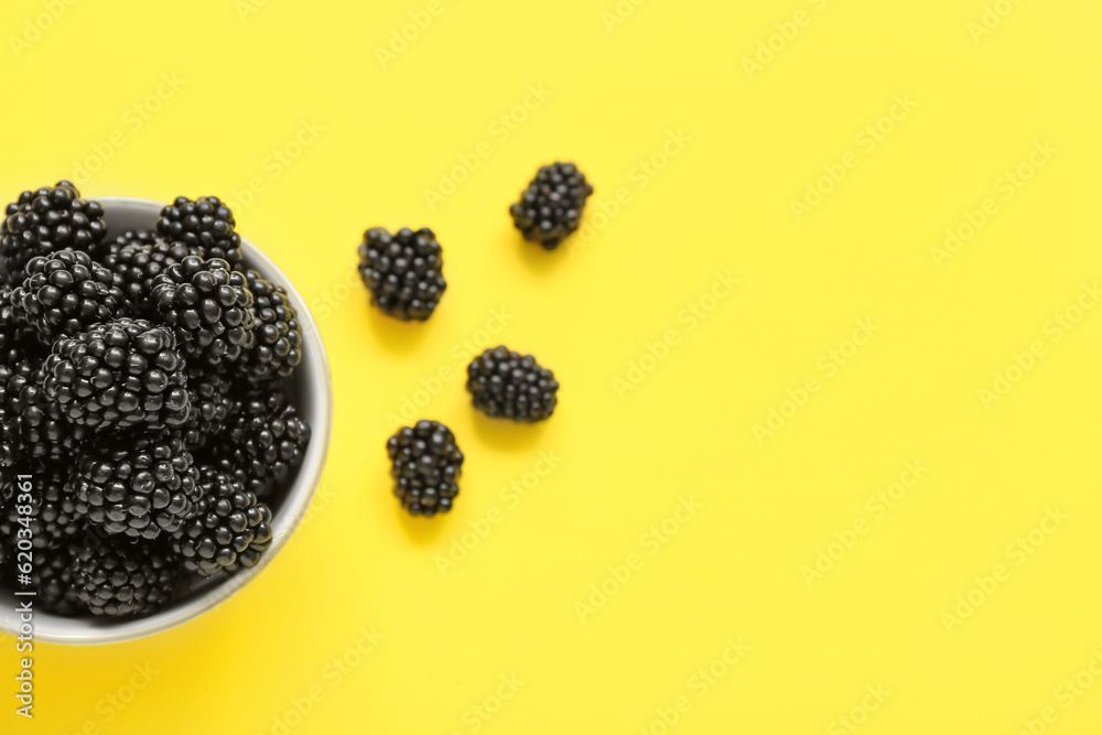 Bowl with fresh blackberry on yellow background, closeup