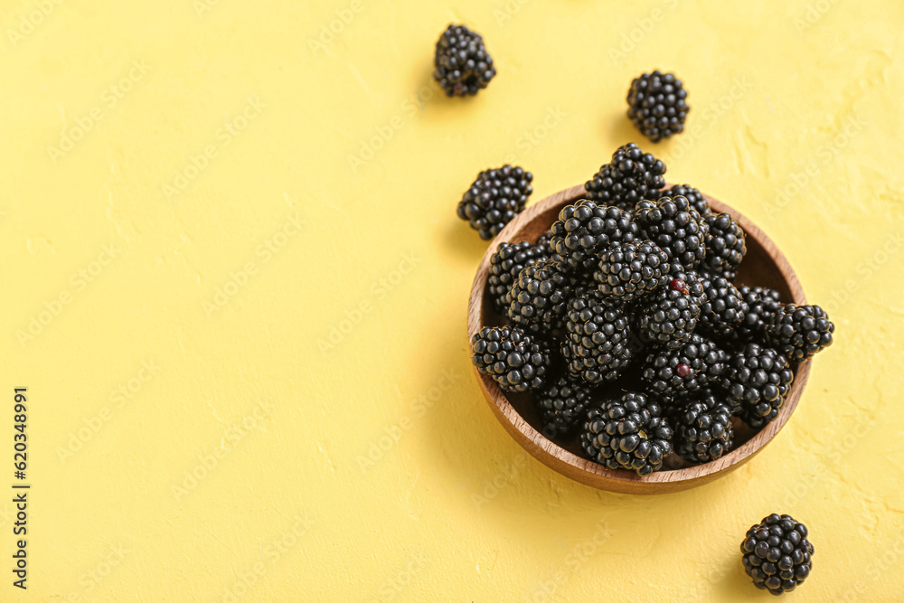 Bowl with fresh blackberry on yellow background, closeup