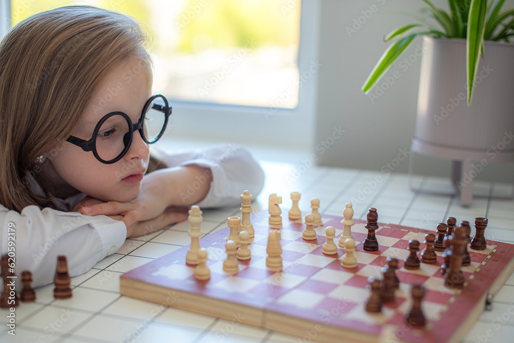 Young girl in glasses playing chess at home, education, strategy game, tactics