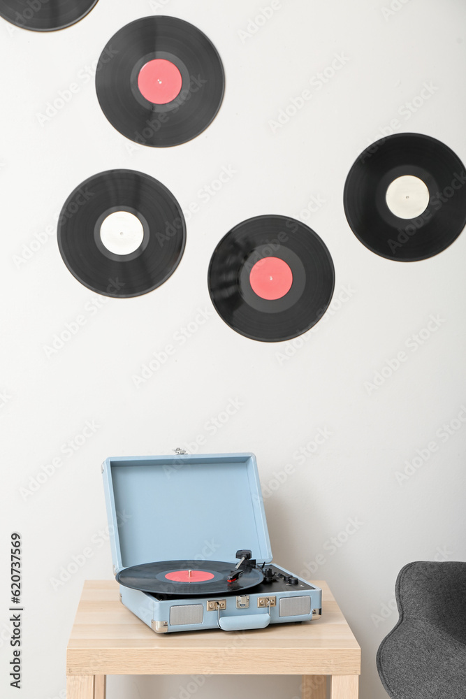 Record player with vinyl disk on table near light wall in room