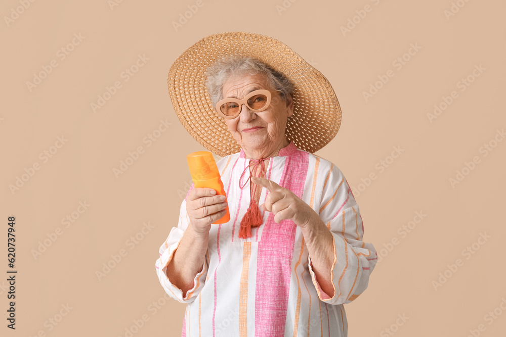 Senior woman pointing at sunscreen cream on beige background