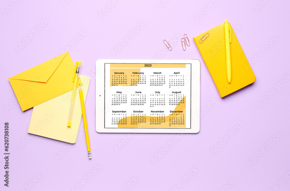 Modern tablet computer with calendar, notebook, envelope and stationary on lilac background