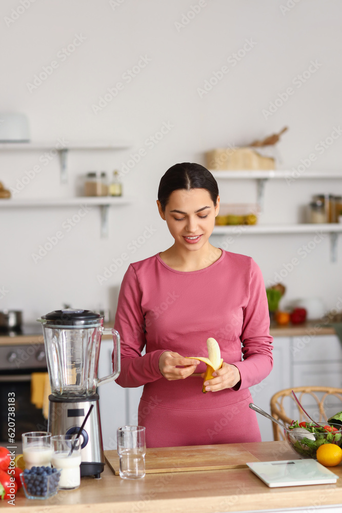 Sporty young woman peeling banana in kitchen