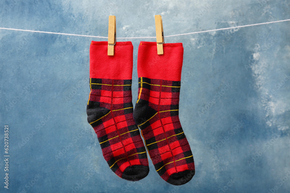 Pair of checkered socks hanging on rope against color background