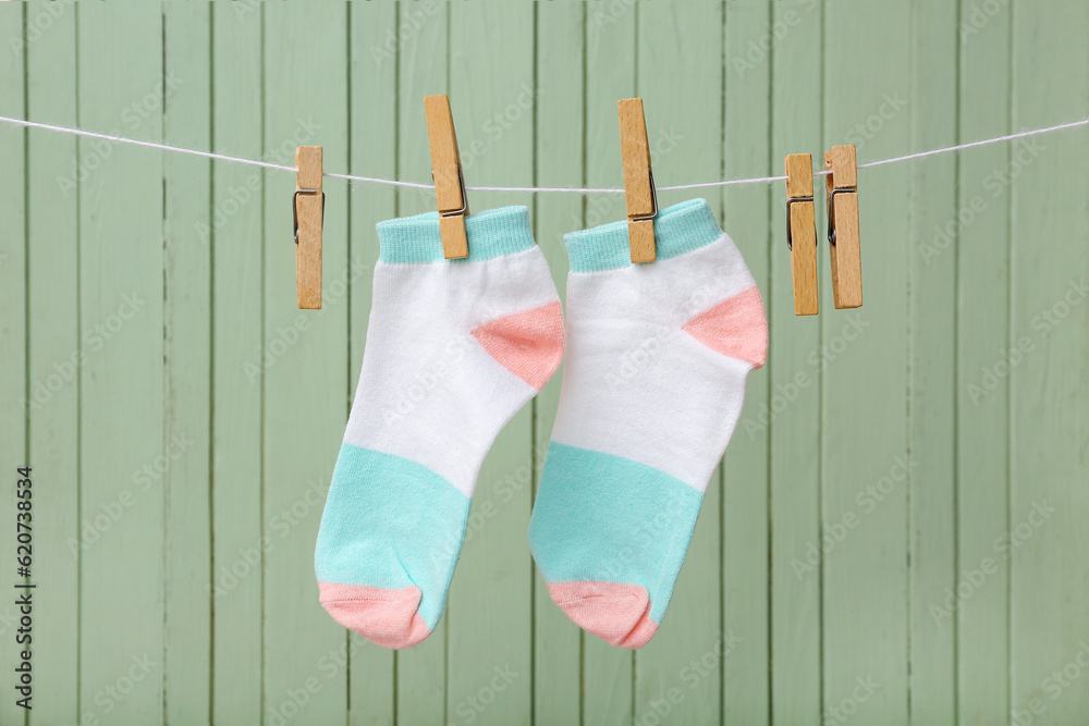 Pair of cotton socks hanging on rope against color wooden background