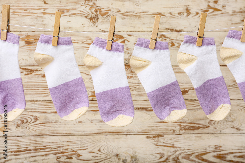 Cotton socks hanging on rope against light wooden background, closeup