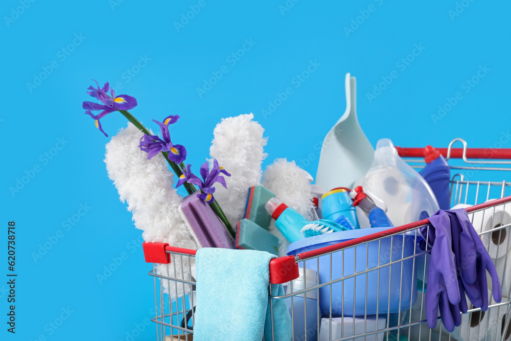 Shopping cart full of cleaning supplies and purple flowers on blue background