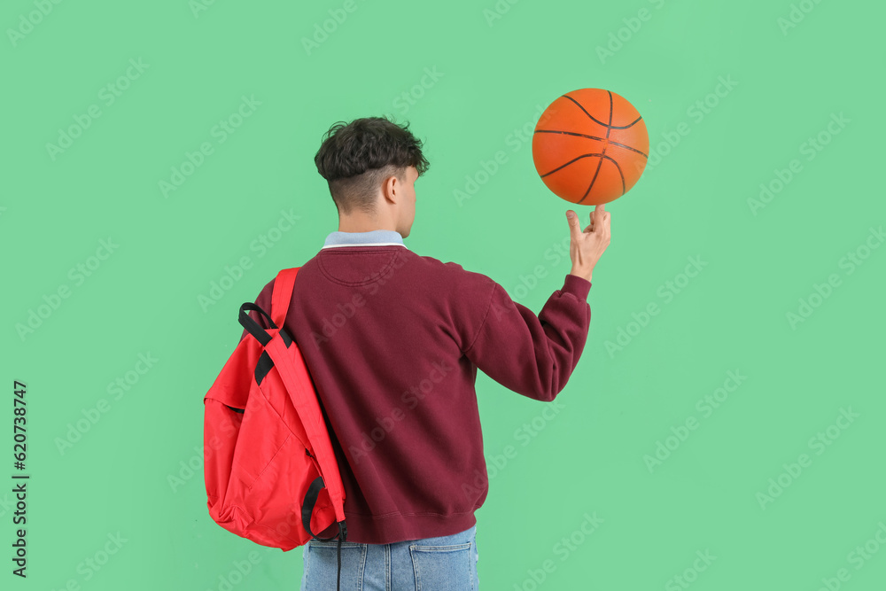 Male student with ball and backpack on green background, back view