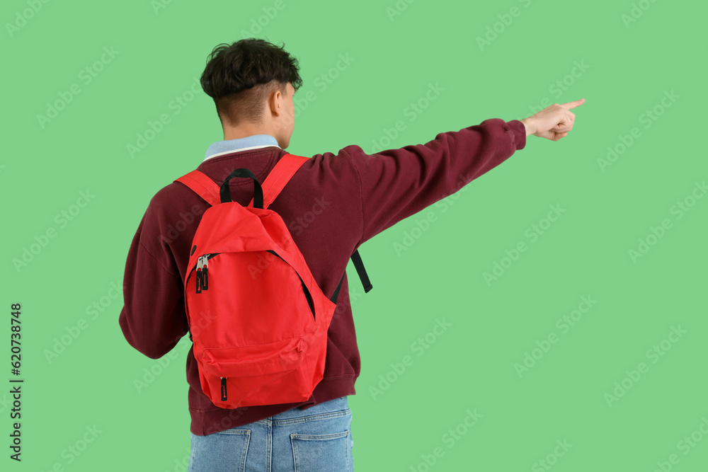 Male student with backpack pointing at something on green background, back view