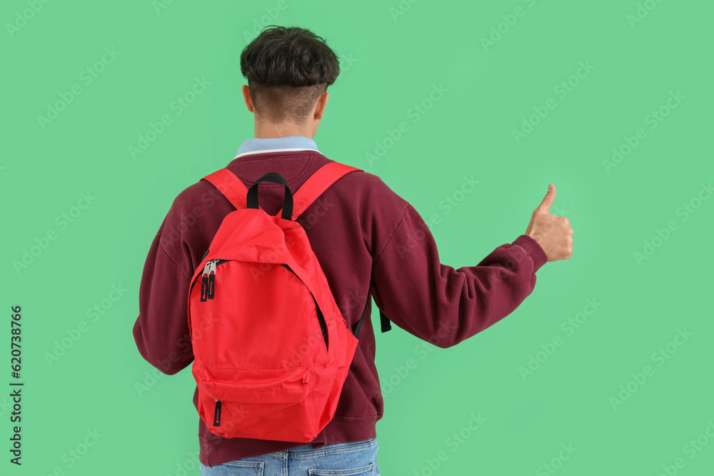 Male student with backpack showing thumb-up on green background, back view