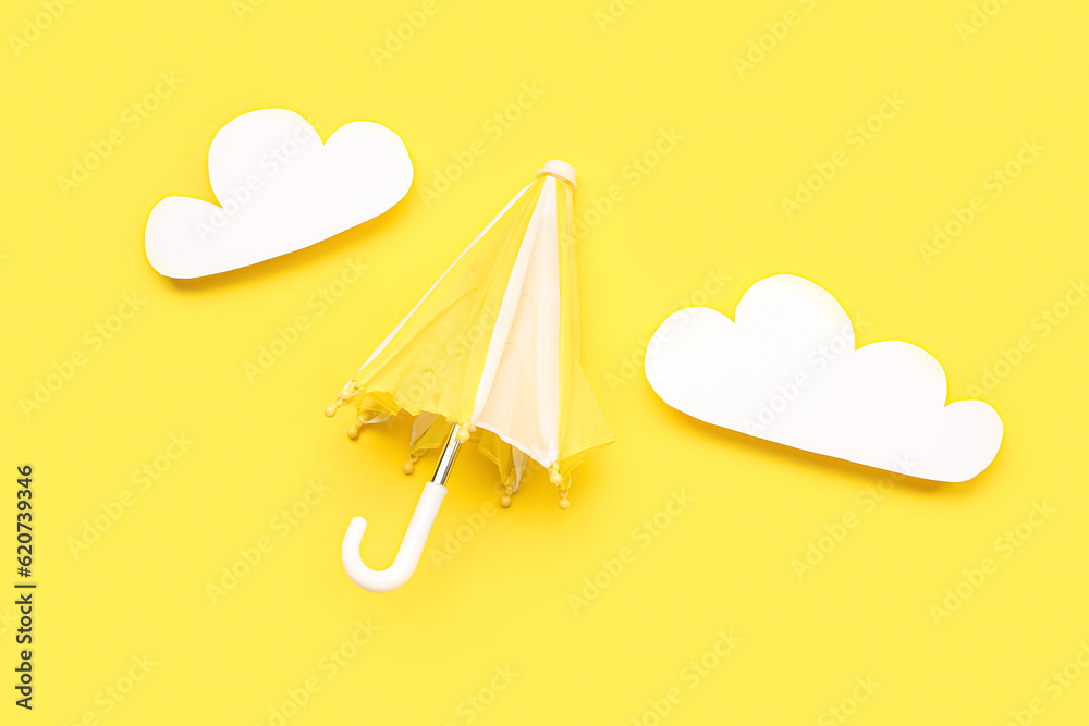 Umbrella with paper clouds on yellow background. Weather forecast concept