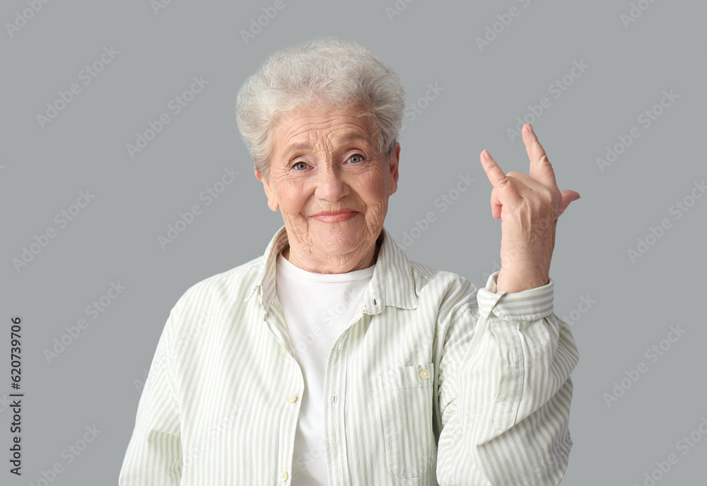 Senior woman showing  i love you  gesture on grey background