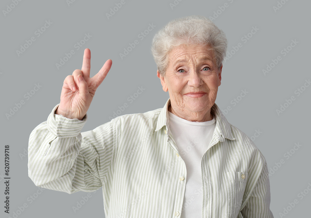 Senior woman showing victory gesture on grey background