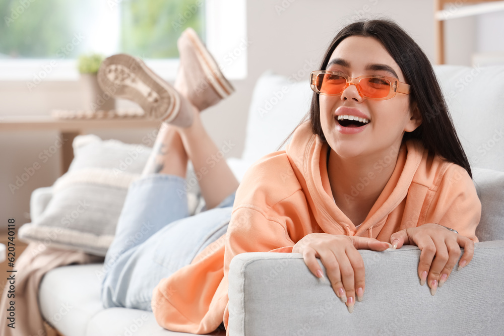 Young woman wearing stylish sunglasses while lying on sofa