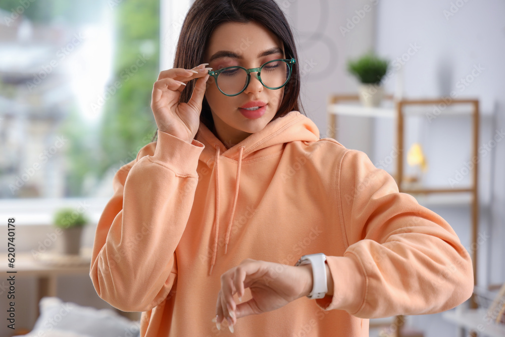 Beautiful young woman wearing glasses and looking at watch at home