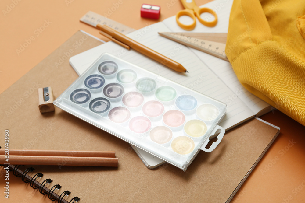 Notebooks, paints and school stationery on orange background, closeup