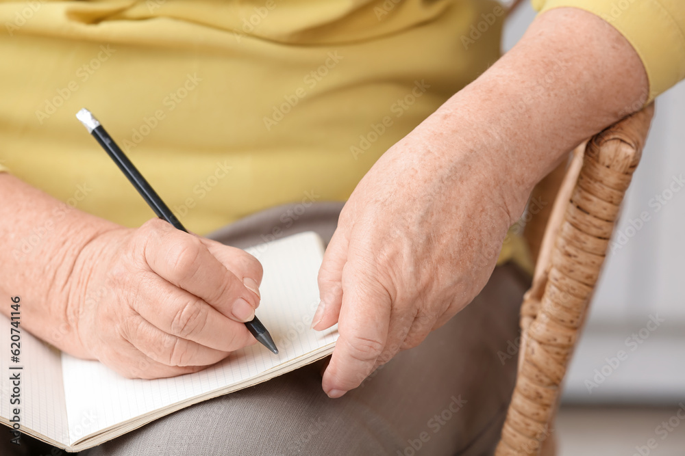 Senior woman writing in notebook at home, closeup