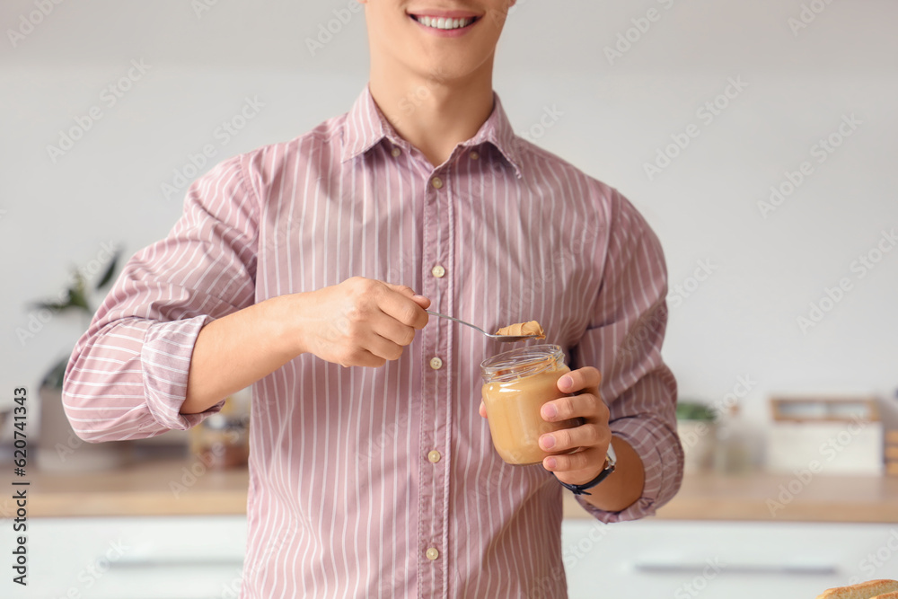 Young man eating tasty nut butter in kitchen