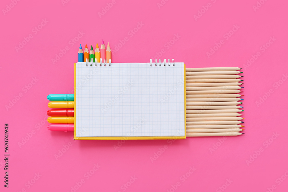 Blank notebook with different colorful markers and pencils on pink background