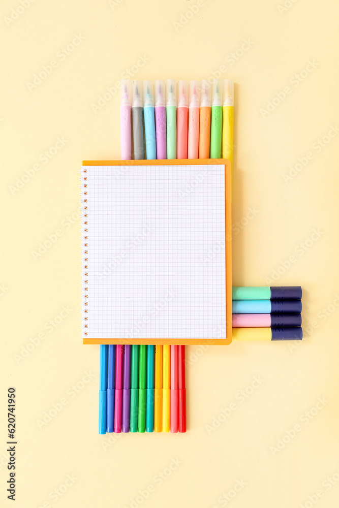 Blank notebook with different colorful markers on pale yellow background