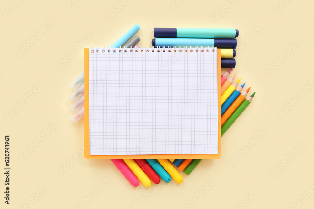 Blank notebook with different colorful markers and pencils on pale yellow background