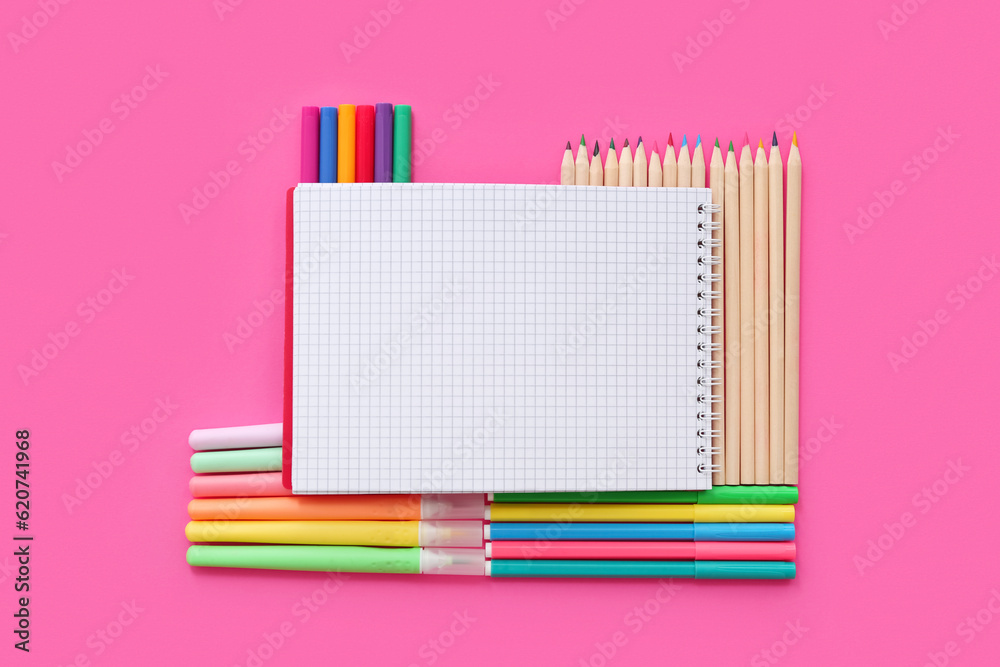 Blank notebook with different colorful markers and pencils on pink background