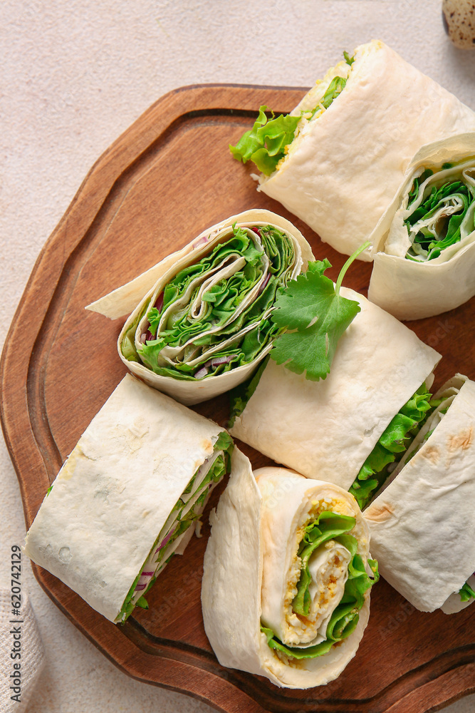 Wooden board of tasty lavash rolls with onion, egg and greens on light background