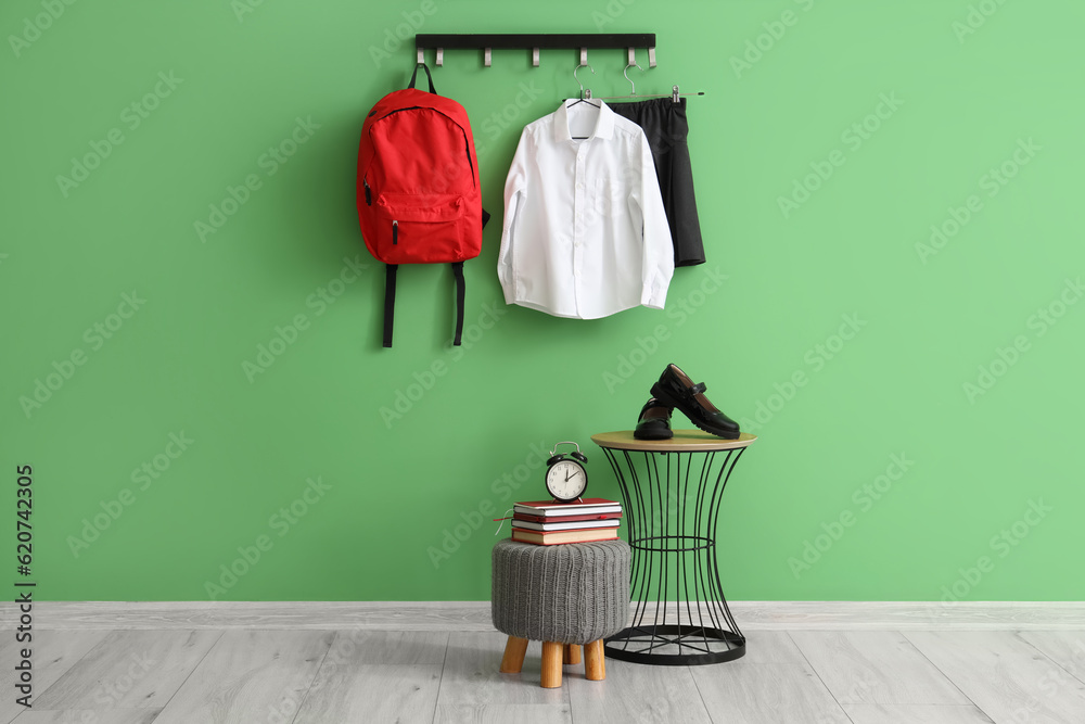 Rack with stylish school uniform, bench and table near green wall in room