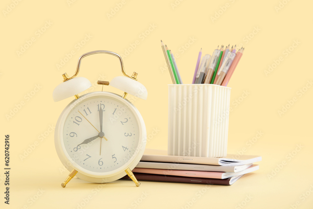 Alarm clock with notebooks and stationery holder on yellow background