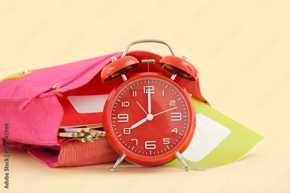 Backpack with alarm clock and different stationery on pale orange background