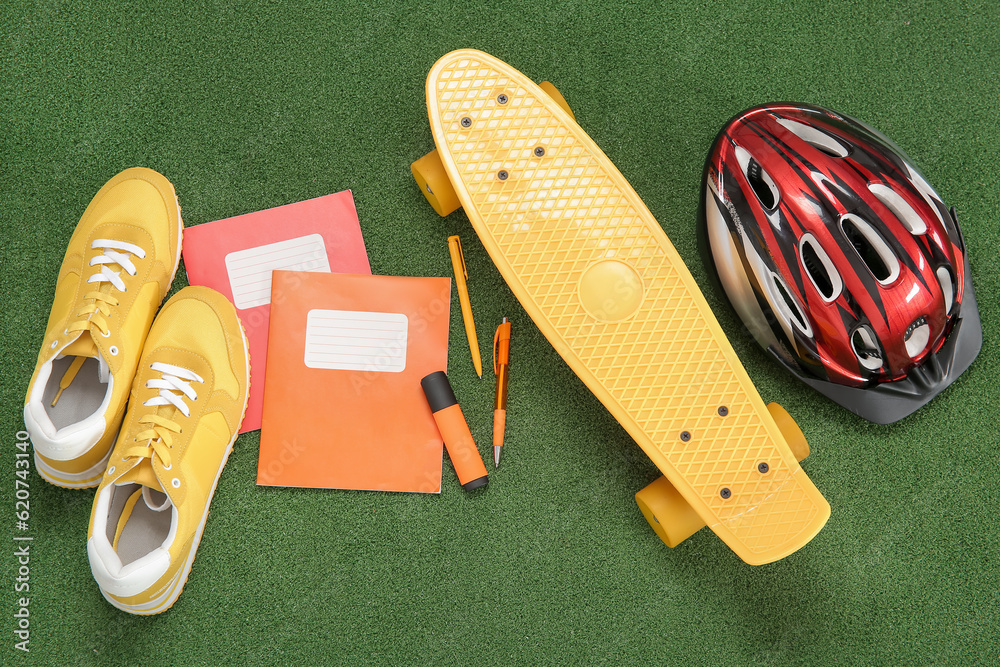 Bike helmet with sneakers, skateboard and different stationery on color background