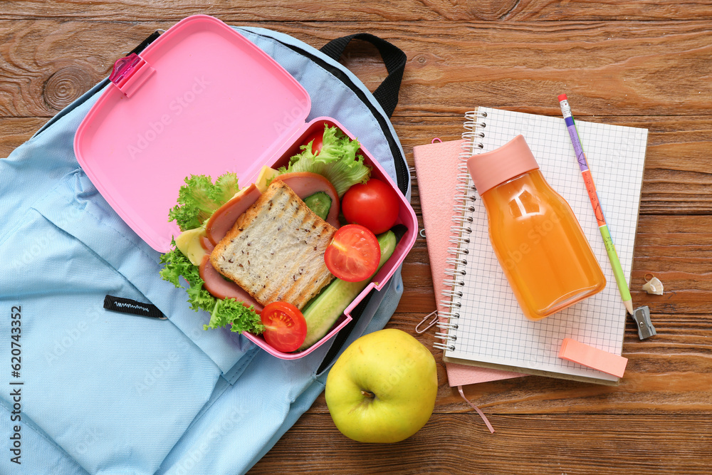 Backpack, stationery, drink and lunch box with tasty food on brown wooden background