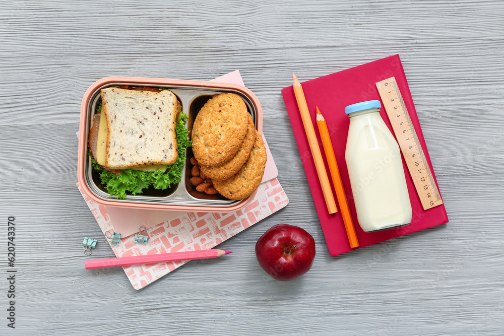 Stationery, drink and lunch box with tasty food on grey wooden background