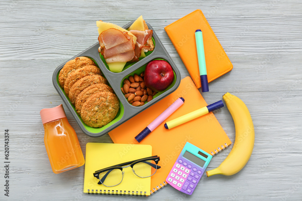 Stationery, drink and lunch box with tasty food on grey wooden background