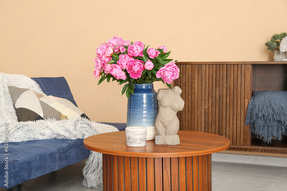 Vase of pink peonies on coffee table, couch and dresser near beige wall