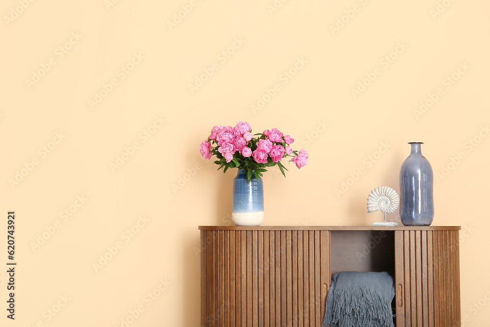 Vase of pink peonies with figurine on dresser near beige wall