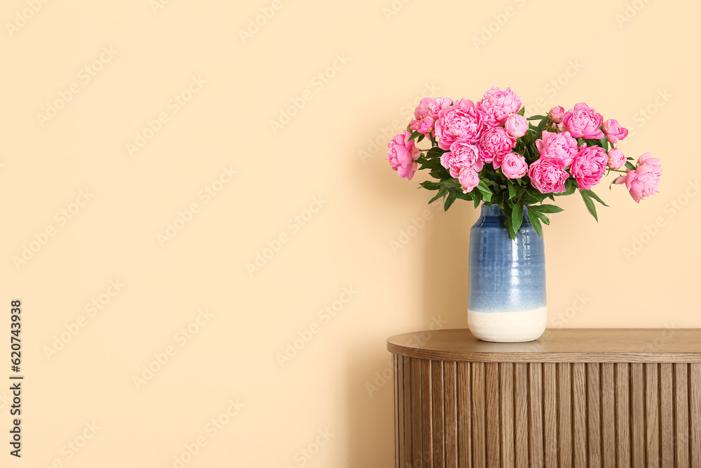 Vase of pink peonies on dresser near beige wall