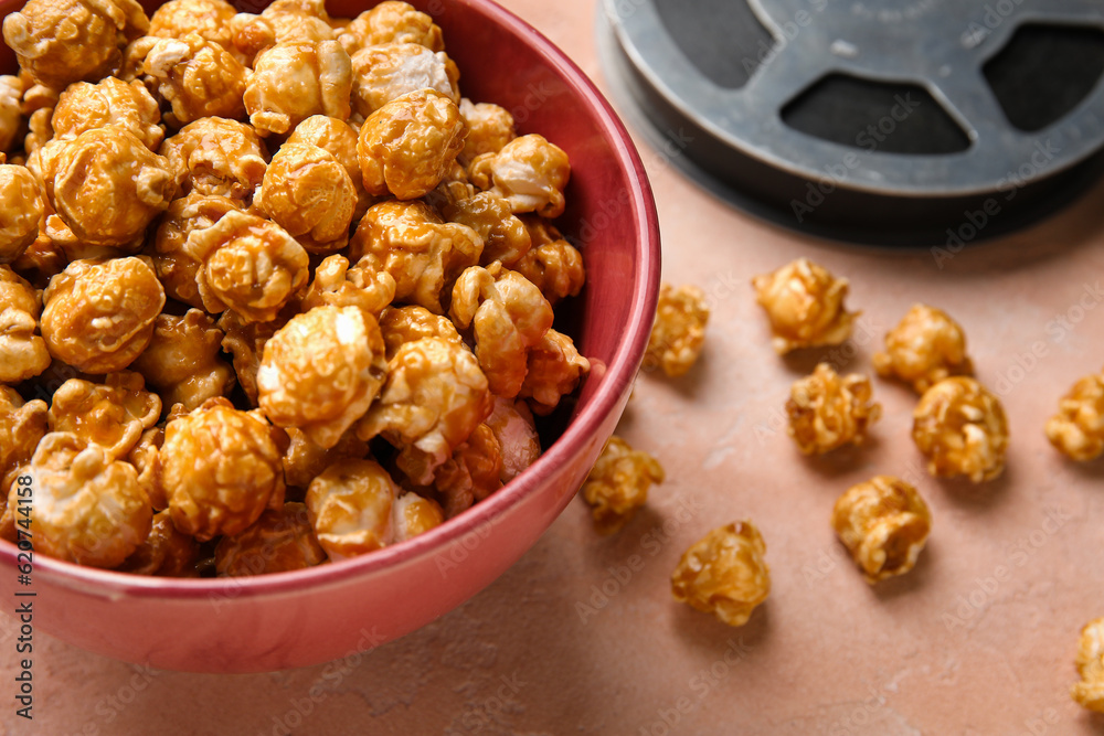 Bowl with tasty popcorn and film reel on pink background