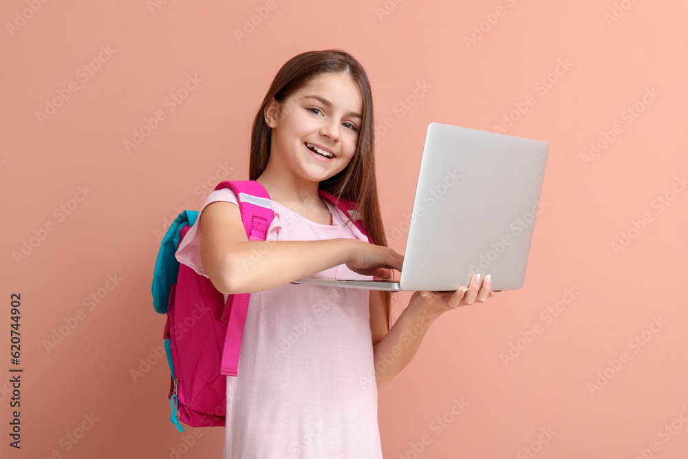 Little girl with backpack using laptop on pink background