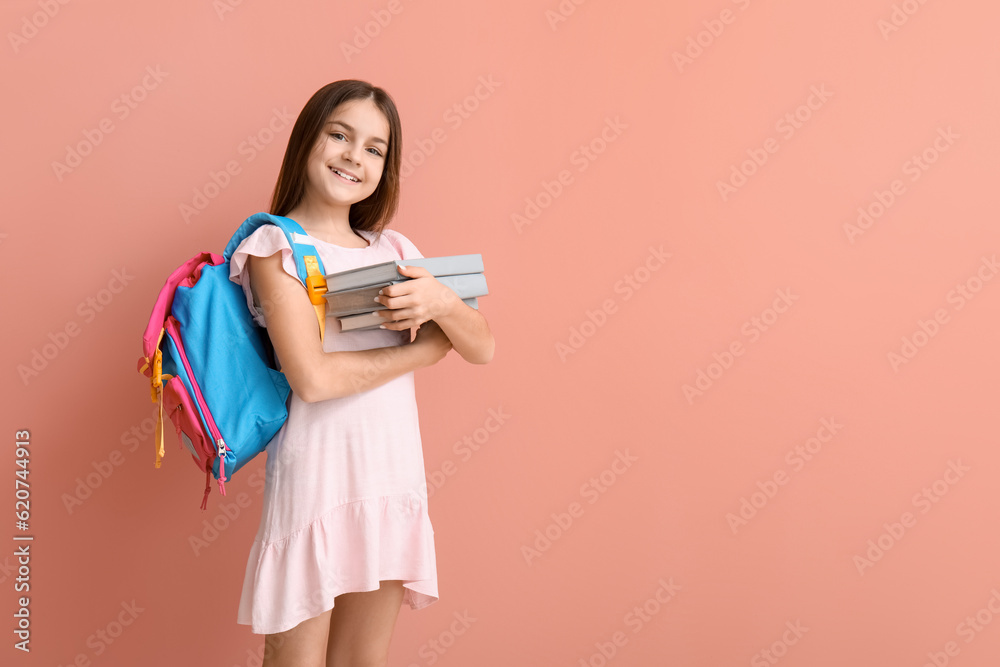 Little girl with books and backpack on pink background