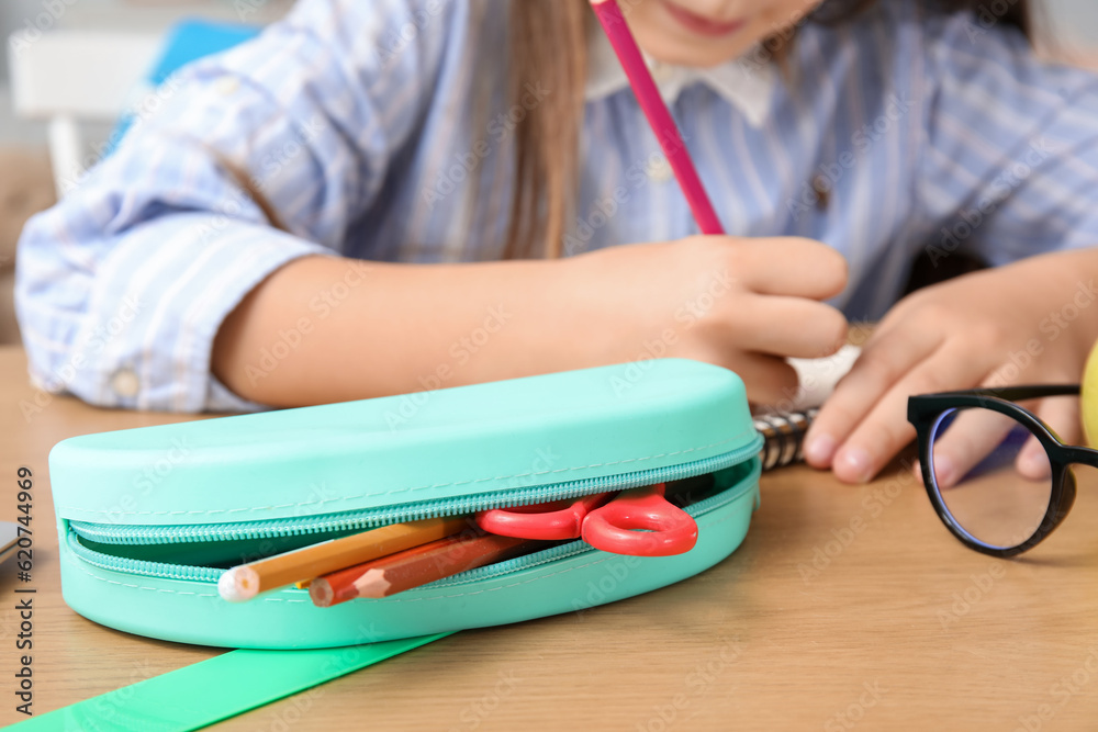 Little girl with pencil case drawing at table, closeup