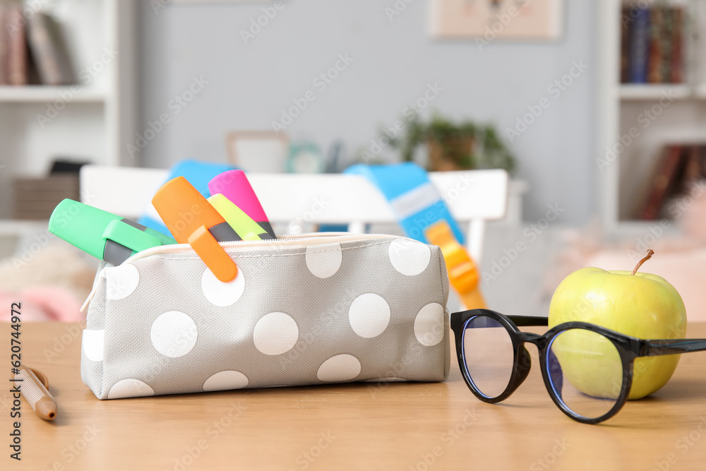 Pencil case with eyeglasses and apple on table in room, closeup