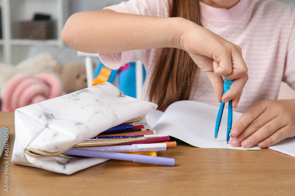 Little girl with pencil case and pair of compasses at table, closeup