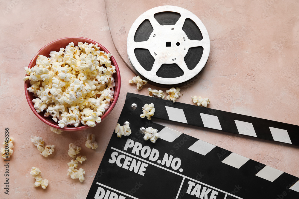 Bowl with tasty popcorn, clapperboard and film reel on light background