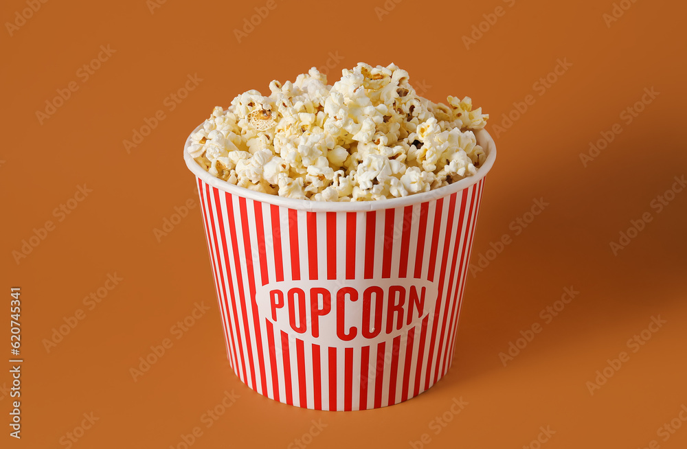 Bucket with tasty popcorn on brown background