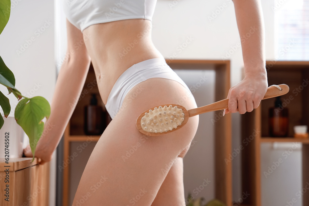 Young woman massaging her buttocks with anti-cellulite brush in bathroom, closeup