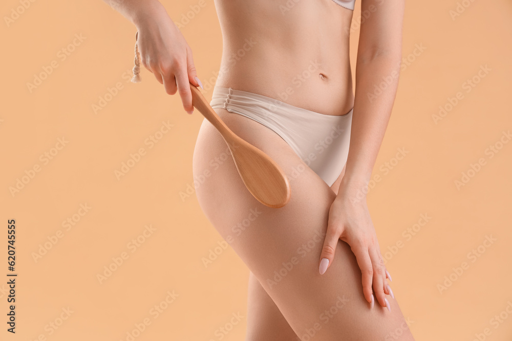 Young woman massaging her buttocks with anti-cellulite brush on beige background, closeup