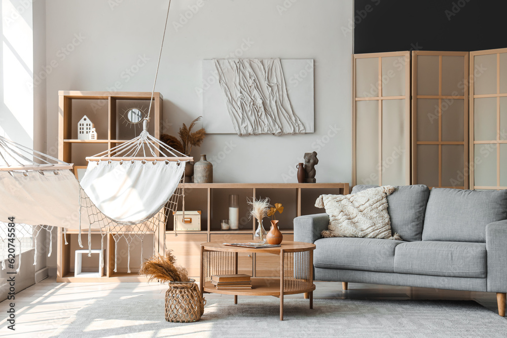 Interior of light living room with hammock, table and sofa