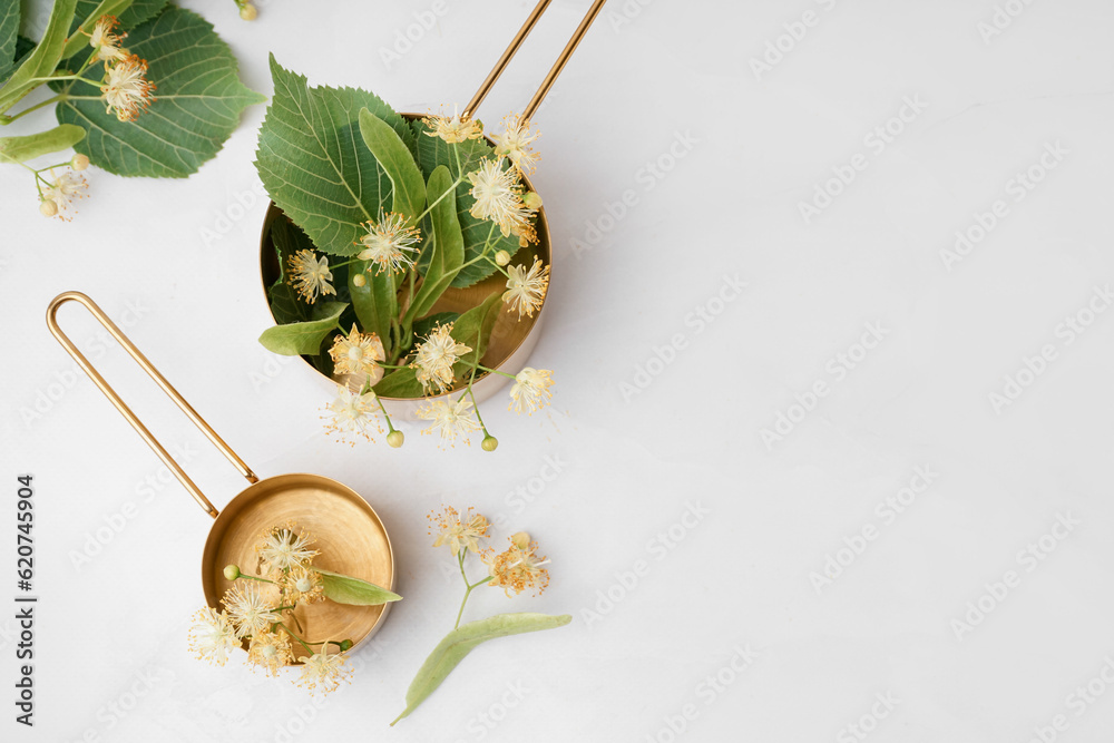 Golden saucepans with aromatic linden flowers on light background