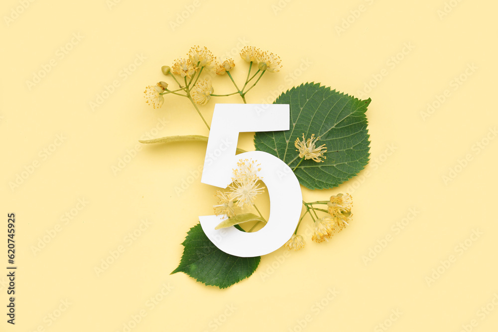 Linden green leaves and flowers with paper number five on yellow background